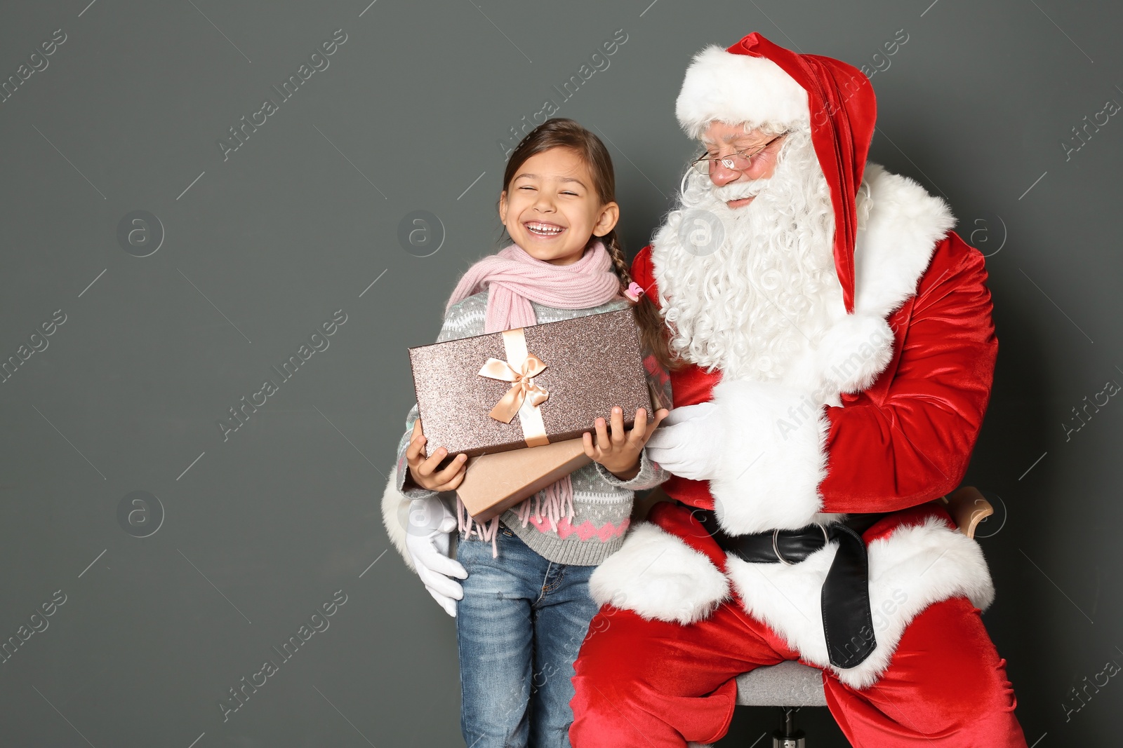 Photo of Little girl with gift box and authentic Santa Claus on grey background