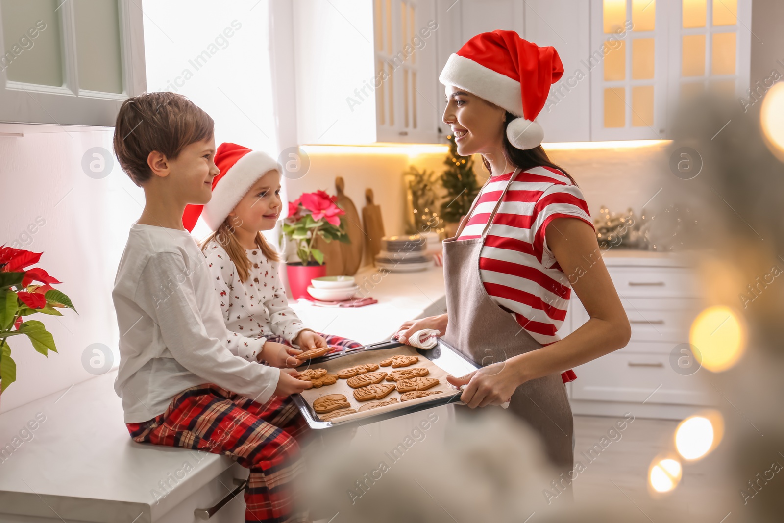 Photo of Mother giving her cute little children freshly baked Christmas cookies in kitchen