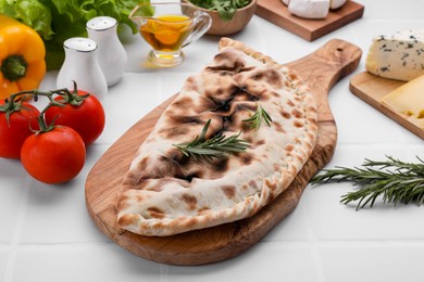 Tasty pizza calzone with rosemary and different products on white tiled table
