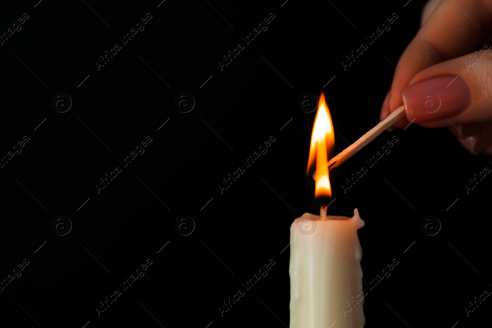 Photo of Woman lighting up candle with match on black background, closeup. Space for text