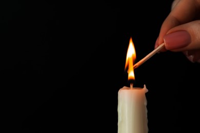 Woman lighting up candle with match on black background, closeup. Space for text