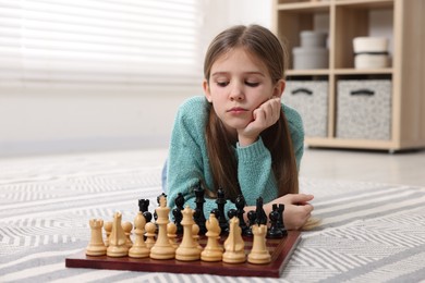 Photo of Cute girl playing chess on floor in room