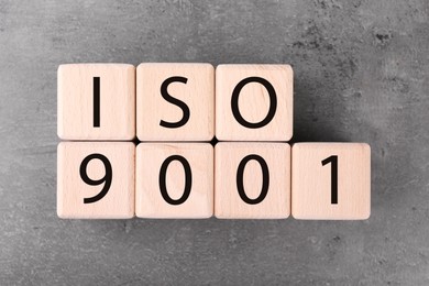 Photo of Wooden cubes with abbreviation ISO and number 9001 on grey textured table, flat lay