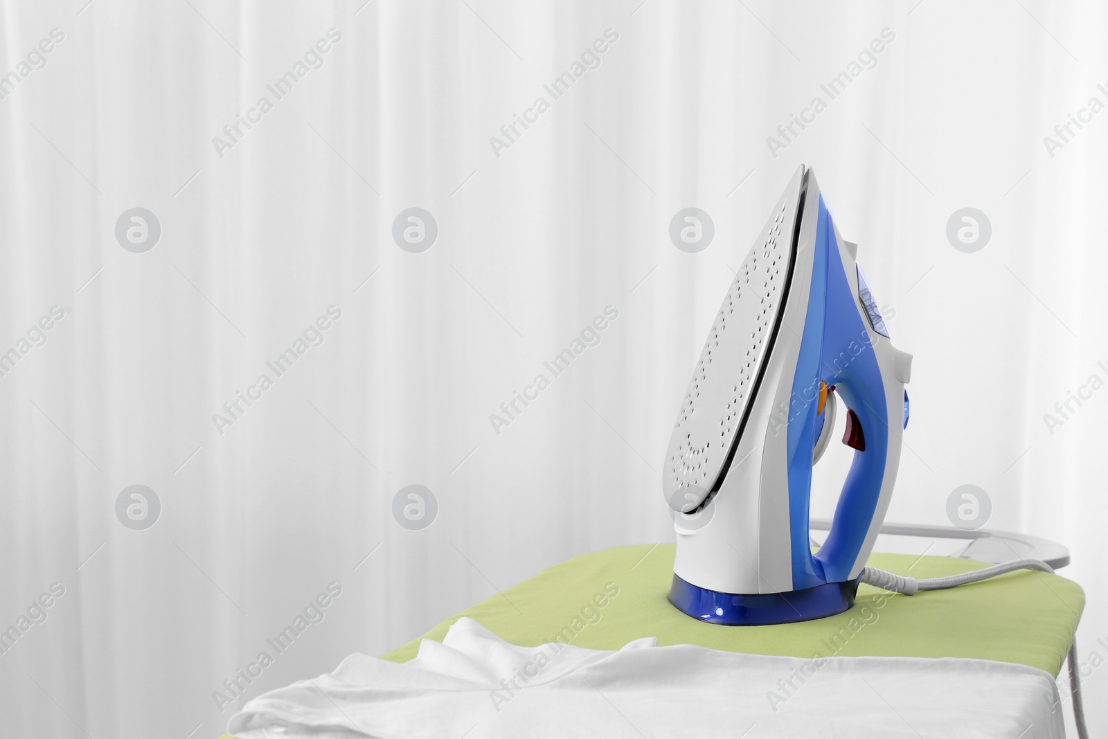 Photo of Modern electric iron and t-shirt on board indoors, space for text. Laundry day