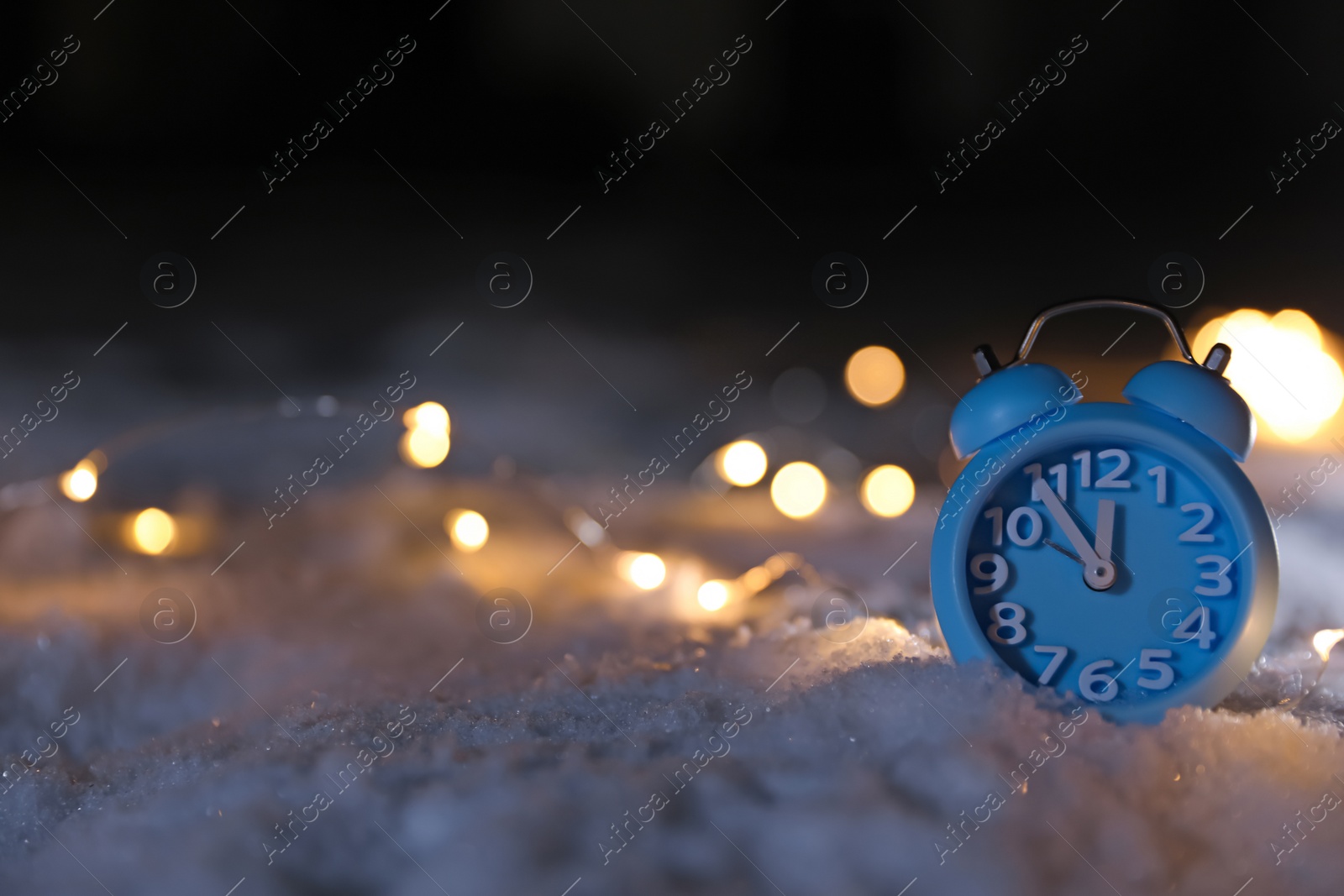 Photo of Alarm clock and Christmas lights on white snow outdoors, space for text. Midnight countdown