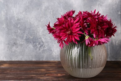 Beautiful pink chrysanthemum flowers in glass vase on wooden table. Space for text