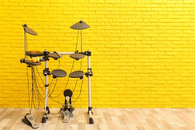 Photo of Modern electronic drum kit near yellow brick wall indoors, space for text. Musical instrument