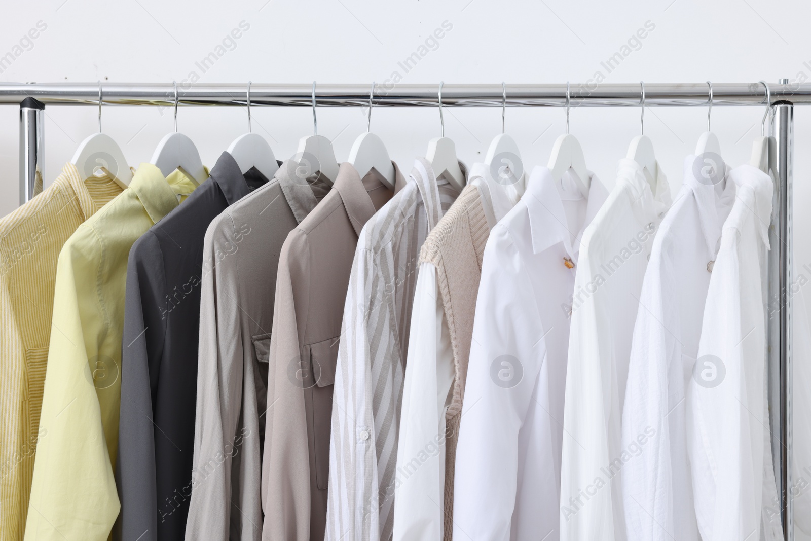 Photo of Rack with different stylish shirts near white wall, closeup. Organizing clothes