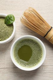 Photo of Cup of fresh matcha tea, bamboo whisk and green powder on wooden table, flat lay