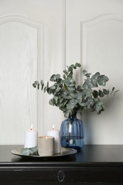 Photo of Eucalyptus branches and burning candles on black table