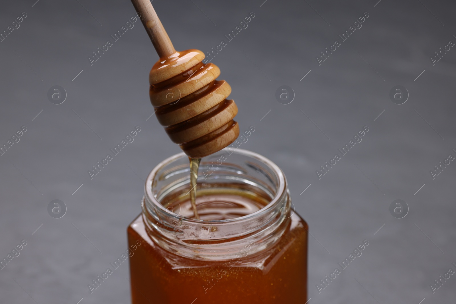 Photo of Pouring sweet honey from dipper into jar at grey table, closeup