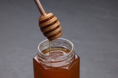 Photo of Pouring sweet honey from dipper into jar at grey table, closeup