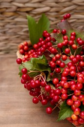 Photo of Wicker basket with ripe red viburnum berries on wooden table, closeup