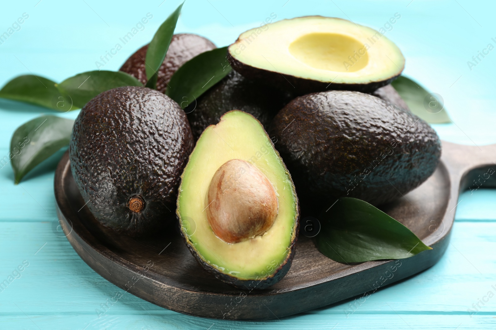 Photo of Board with whole and cut avocados on turquoise table, closeup