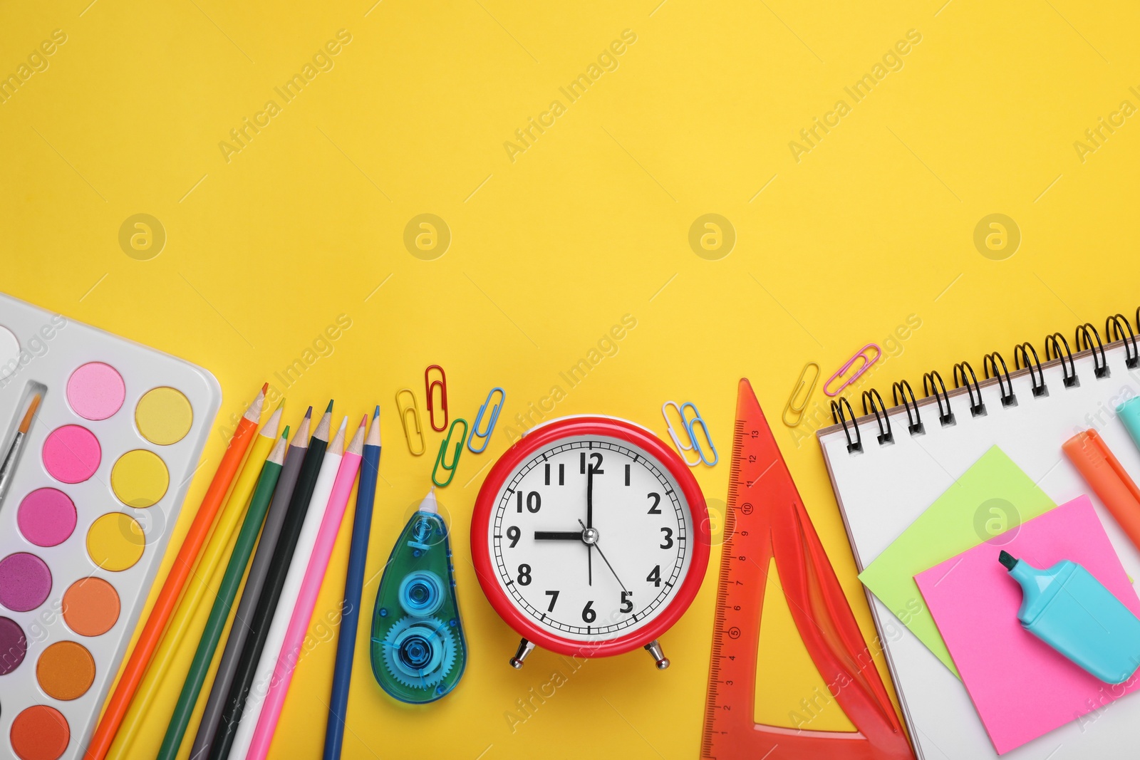 Photo of Flat lay composition with different school stationery and alarm clock on yellow background, space for text. Back to school