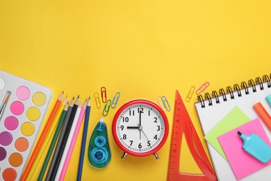 Flat lay composition with different school stationery and alarm clock on yellow background, space for text. Back to school