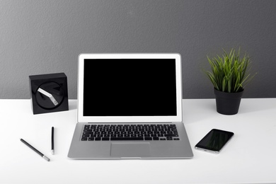 Photo of Modern laptop on table against gray wall. Mock up with space for text