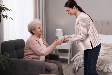 Young caregiver giving tea to senior woman in room. Home care service