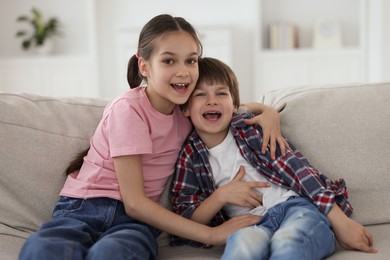 Happy brother and sister spending time together on sofa at home