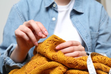 Photo of Woman sewing sweater with needle, closeup view