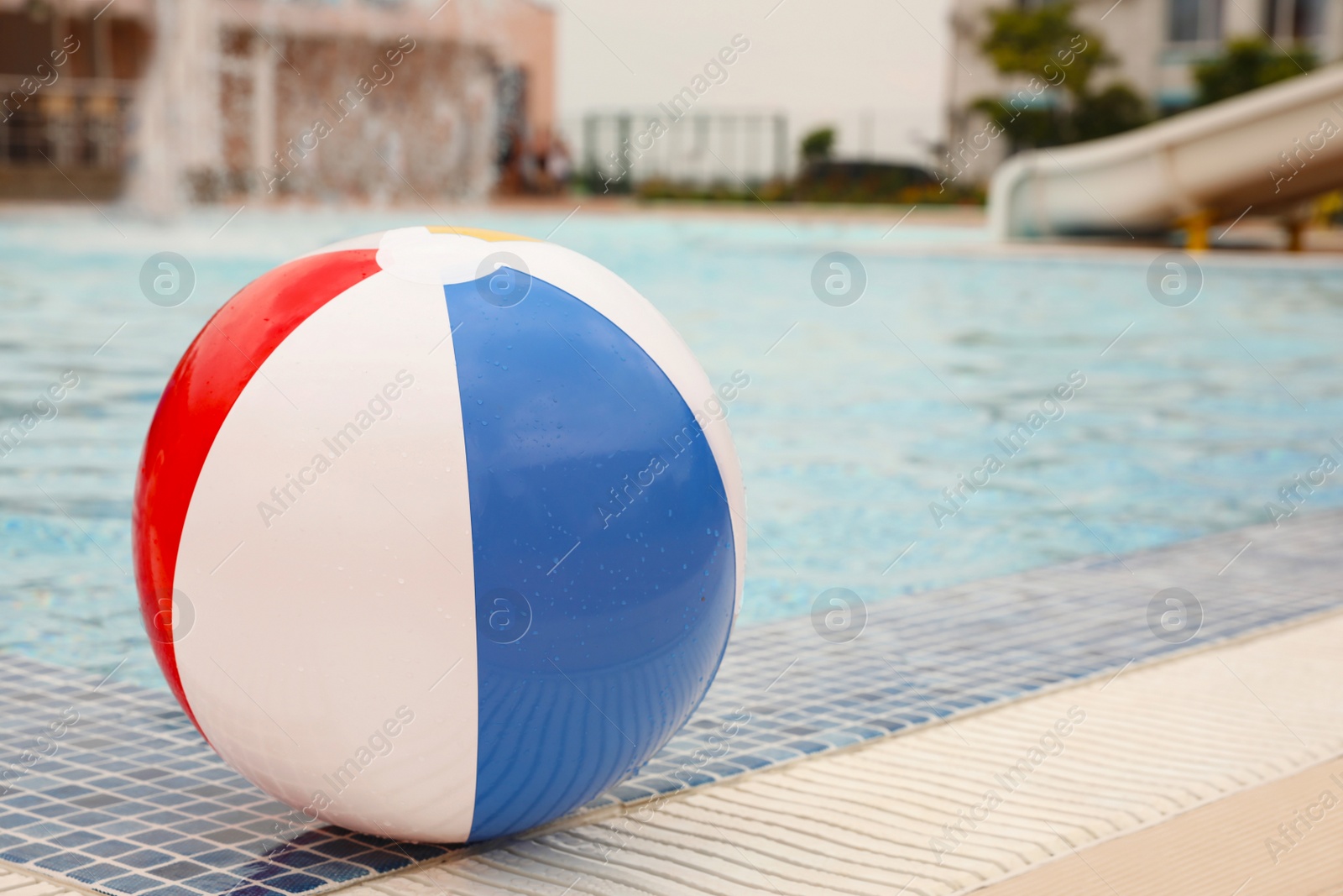 Photo of Inflatable colorful beach ball on edge of outdoor swimming pool, space for text