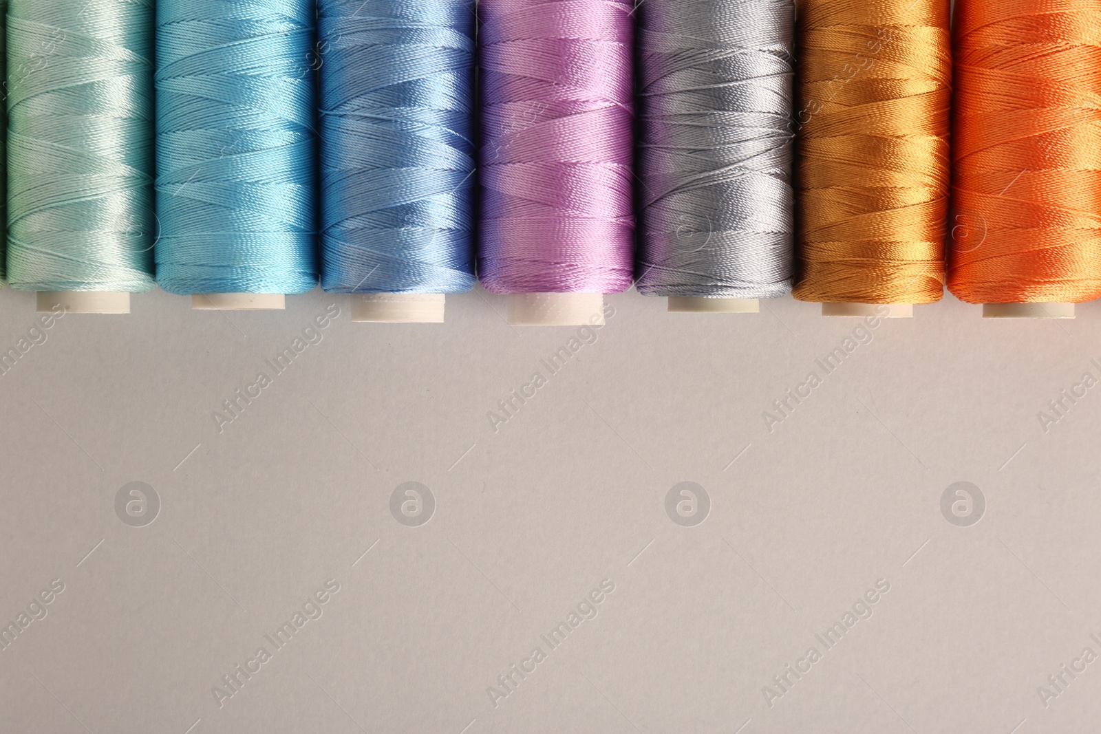 Photo of Different colorful sewing threads on light grey background, flat lay. Space for text