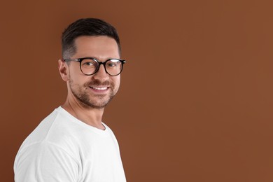 Photo of Portrait of happy man in stylish glasses on brown background. Space for text