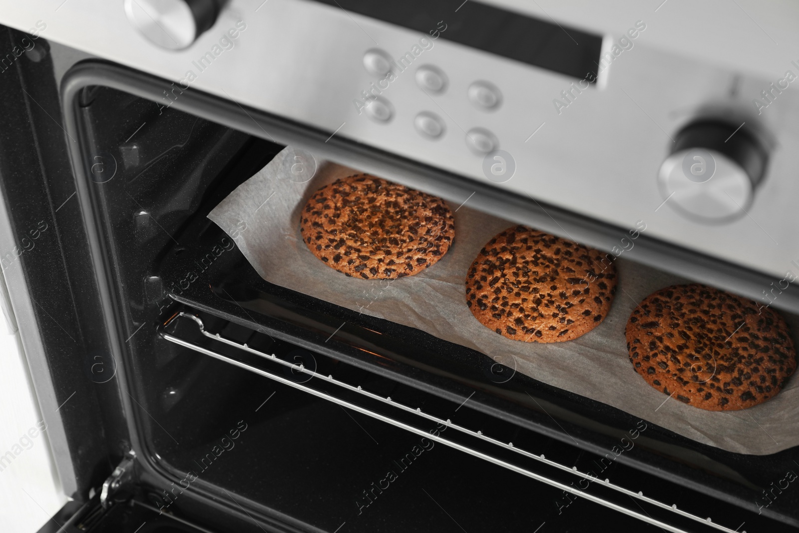 Photo of Open modern oven with freshly baked cookies on sheet, closeup