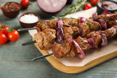 Metal skewers with delicious meat and onion served on blue wooden table, closeup