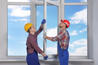 Photo of Workers in uniform installing plastic window indoors
