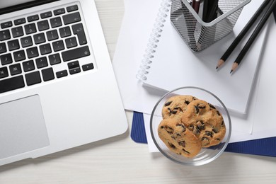 Photo of Bowl with chocolate chip cookies, laptop and office supplies on white wooden table, flat lay