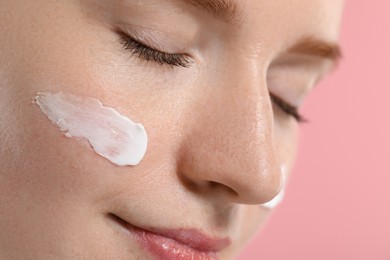 Photo of Beautiful woman with freckles and cream on her face against pink background, closeup