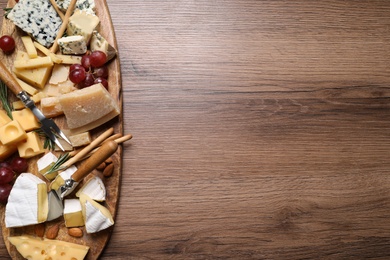 Photo of Cheese plate with rosemary, grapes and nuts on wooden table, top view. Space for text