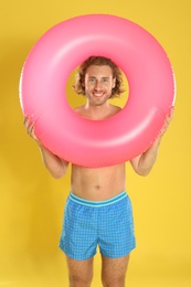 Photo of Attractive young man in beachwear with pink inflatable ring on yellow background