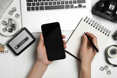 Journalist with smartphone working at white table, top view