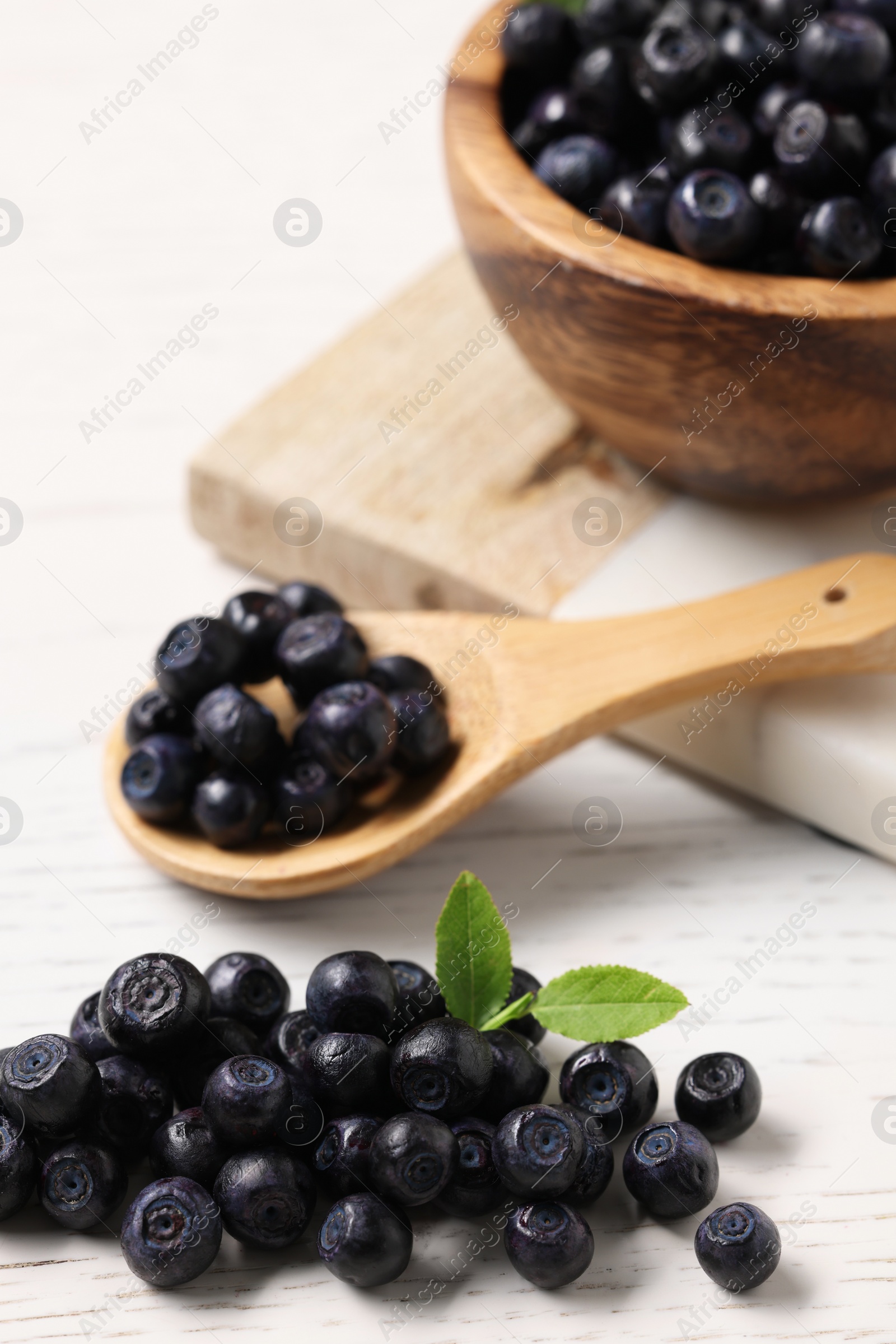 Photo of Ripe bilberries and leaves on white wooden table, selective focus