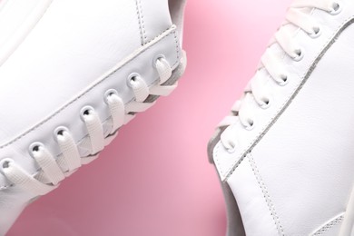 Pair of stylish white sneakers on pink background, top view