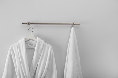 Photo of Hanger with clean bathrobe and towel on light wall