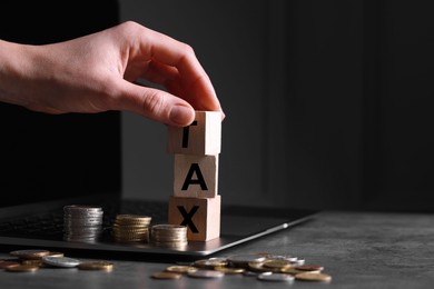 Photo of Woman with word Tax made of wooden cubes, laptop and coins at grey table, closeup. Space for text