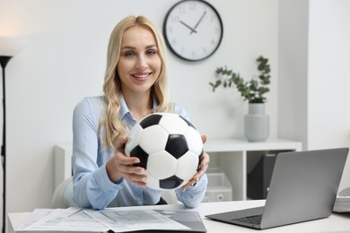 Happy woman with soccer ball at table in office