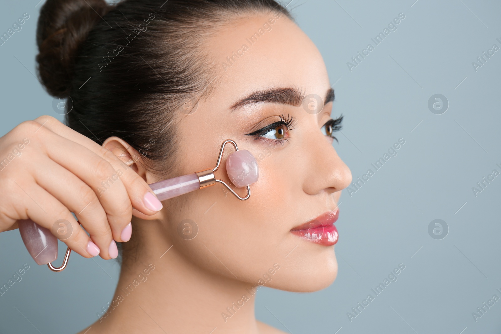 Photo of Woman using natural pink quartz face roller on grey background, closeup. Space for text