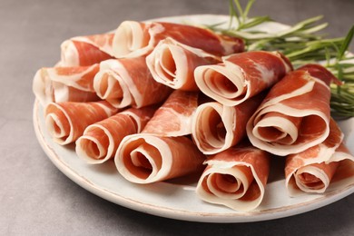 Photo of Rolled slices of delicious jamon with rosemary on grey table, closeup