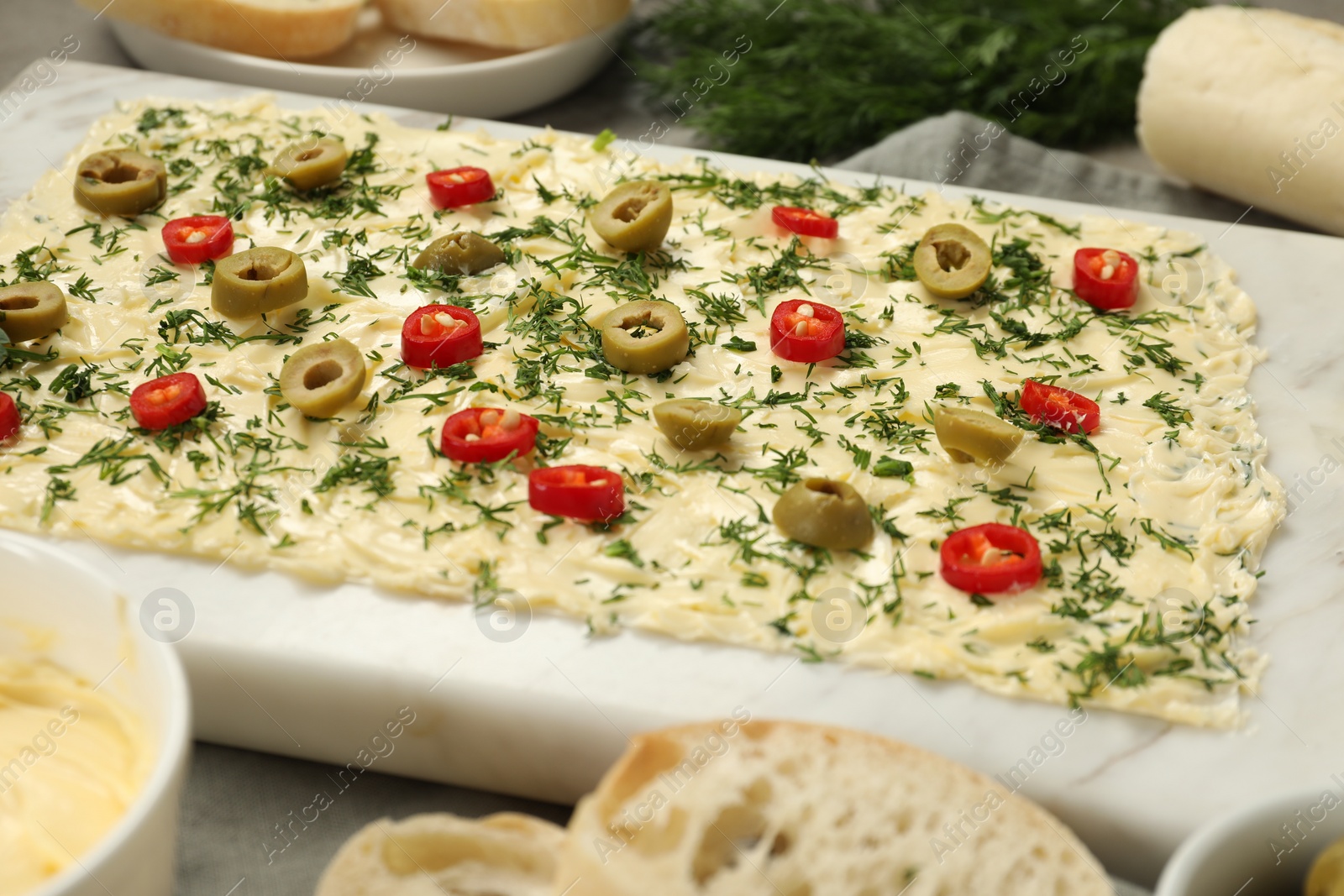 Photo of Fresh butter board with cut olives, dill and pepper on grey table, closeup