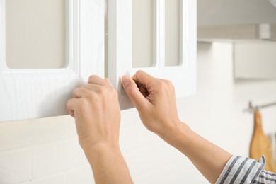 Woman opening cabinet doors at home, closeup