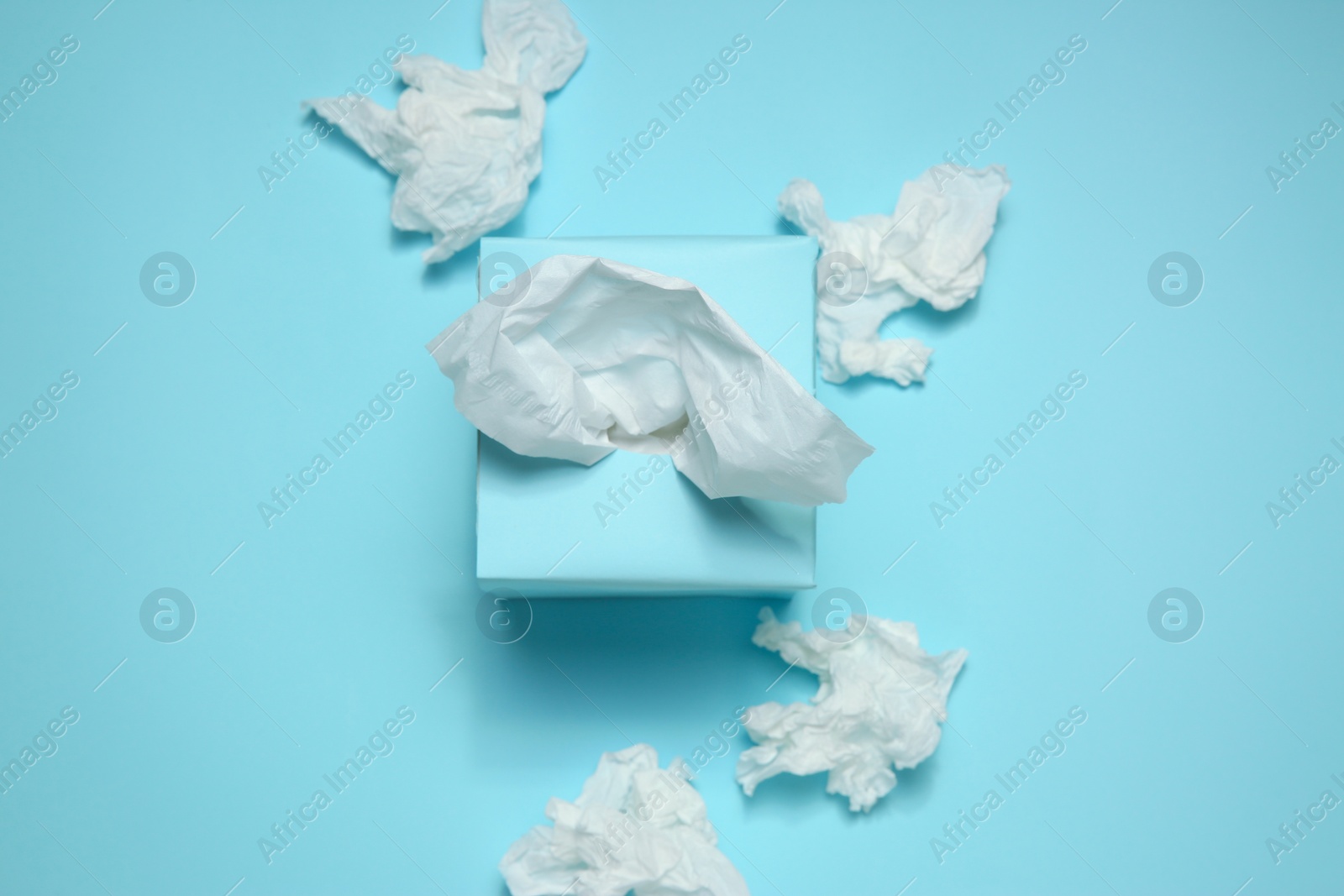 Photo of Used paper tissues and box on light blue background, flat lay