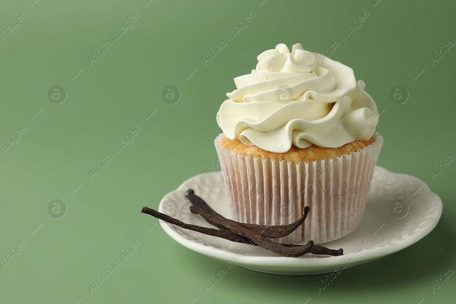 Photo of Tasty cupcake with cream and vanilla pods on green background, space for text