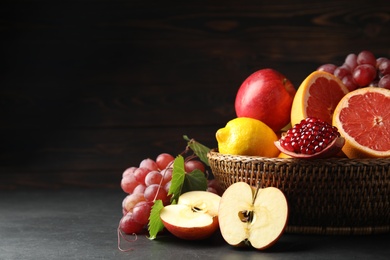 Wicker basket with different fruits on black table. Space for text