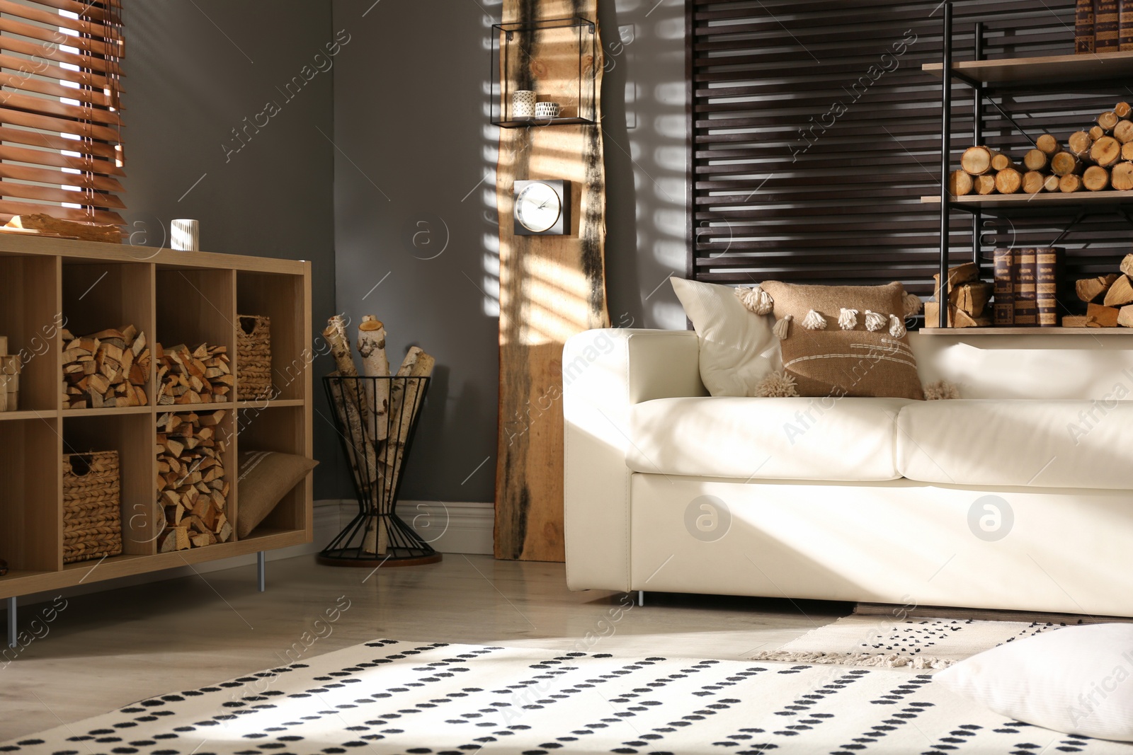 Photo of Shelving unit with stacked firewood and comfortable sofa in stylish room interior