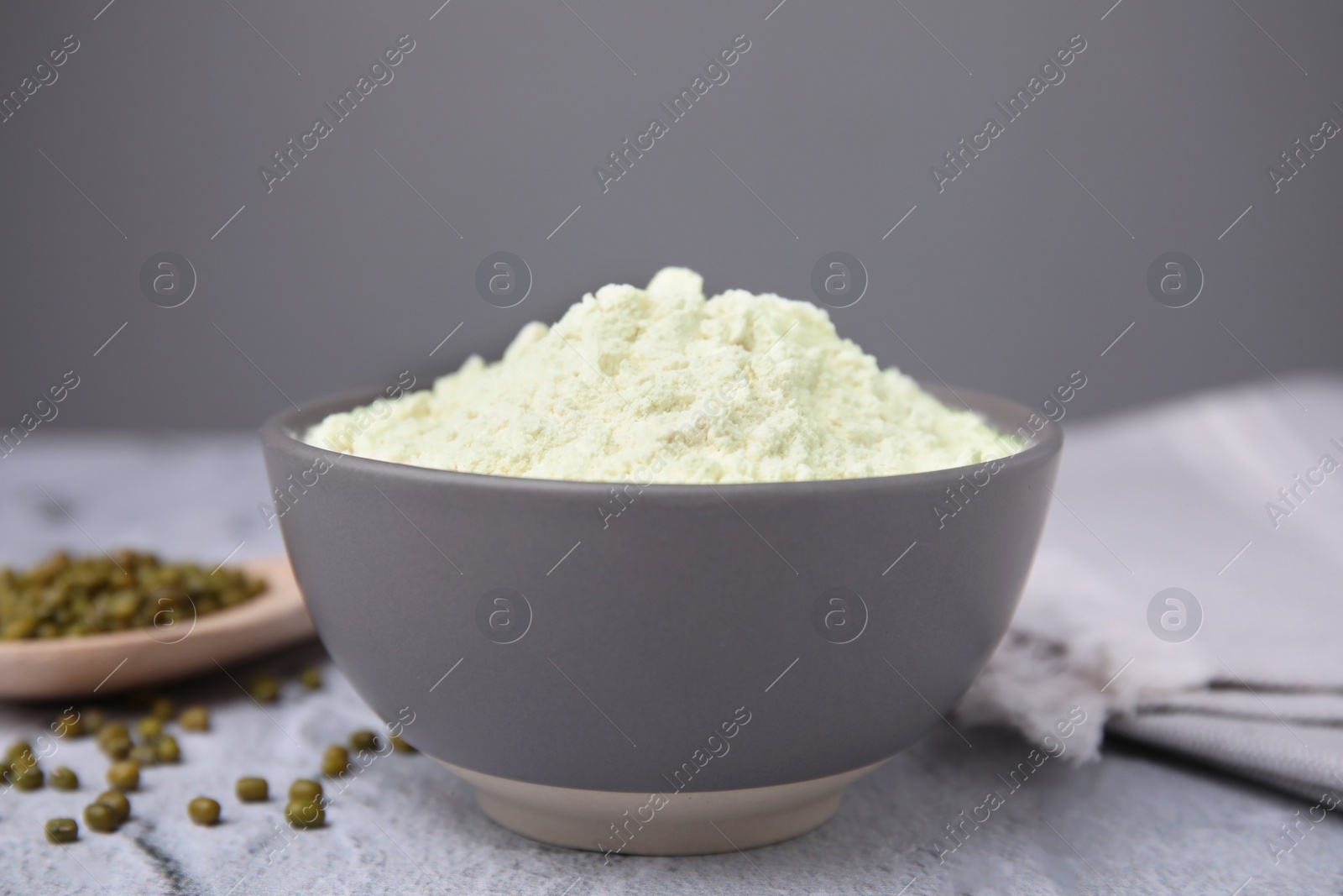 Photo of Mung bean flour in bowl and seeds on white textured table