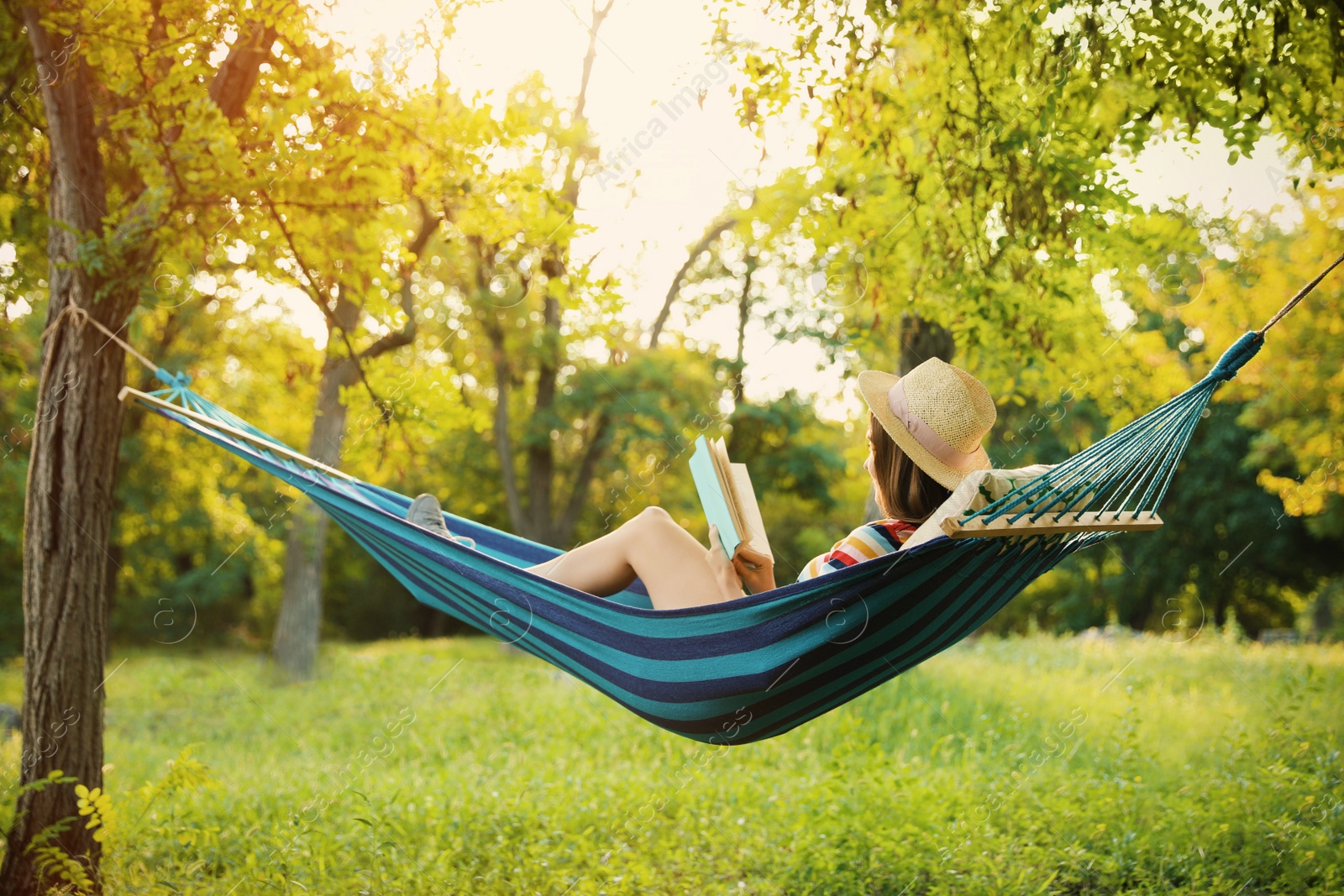 Photo of Young woman reading book in comfortable hammock at green garden